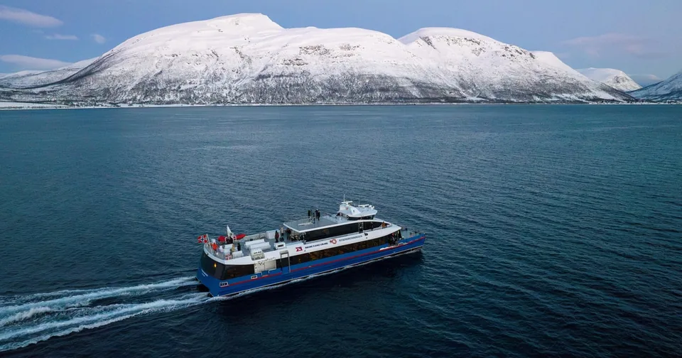 A catamaran crossing a blue fjord below snowy mountains